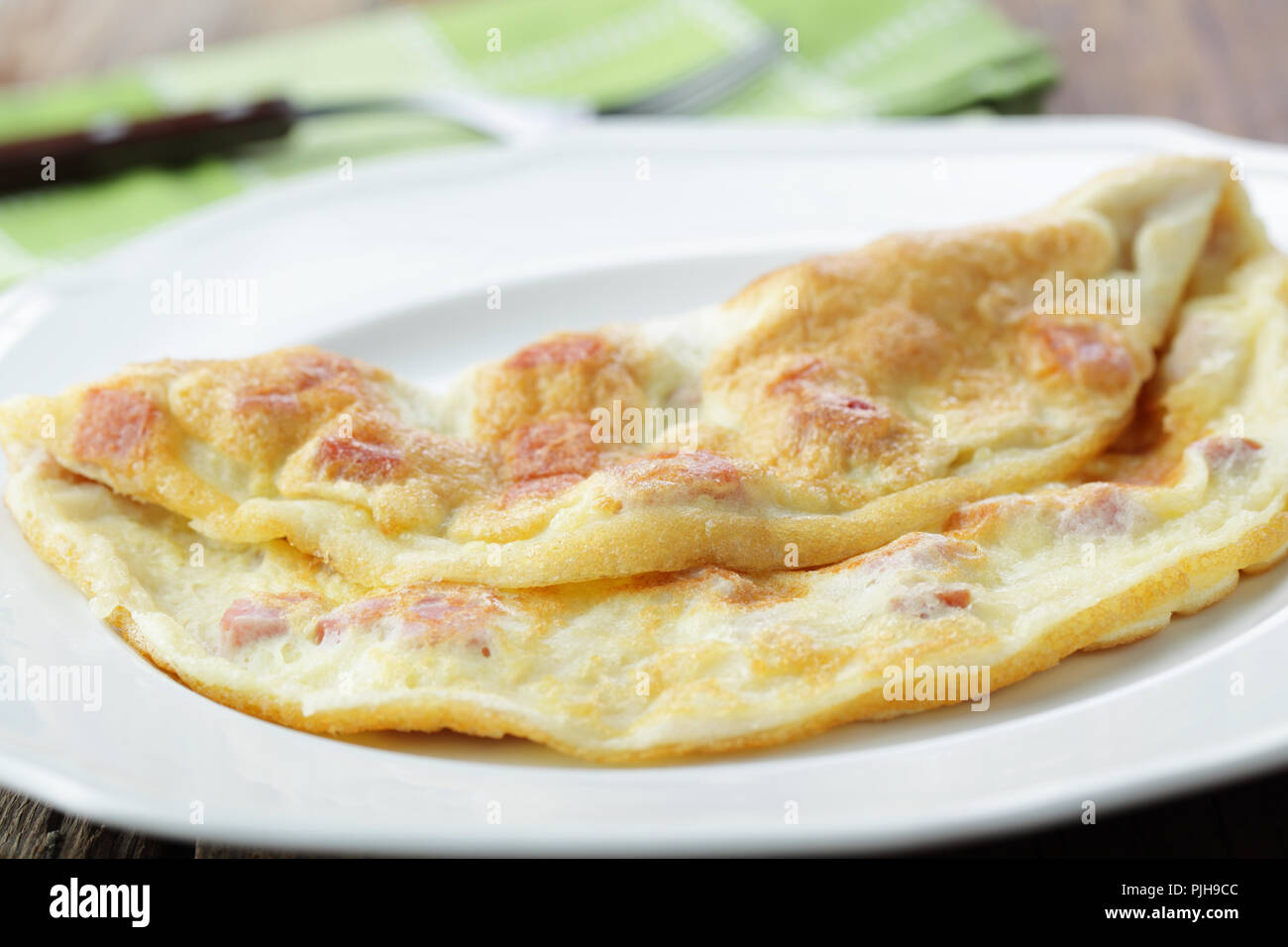 Folded french omelet with pieces of ham on the white plate closeup Stock Photo