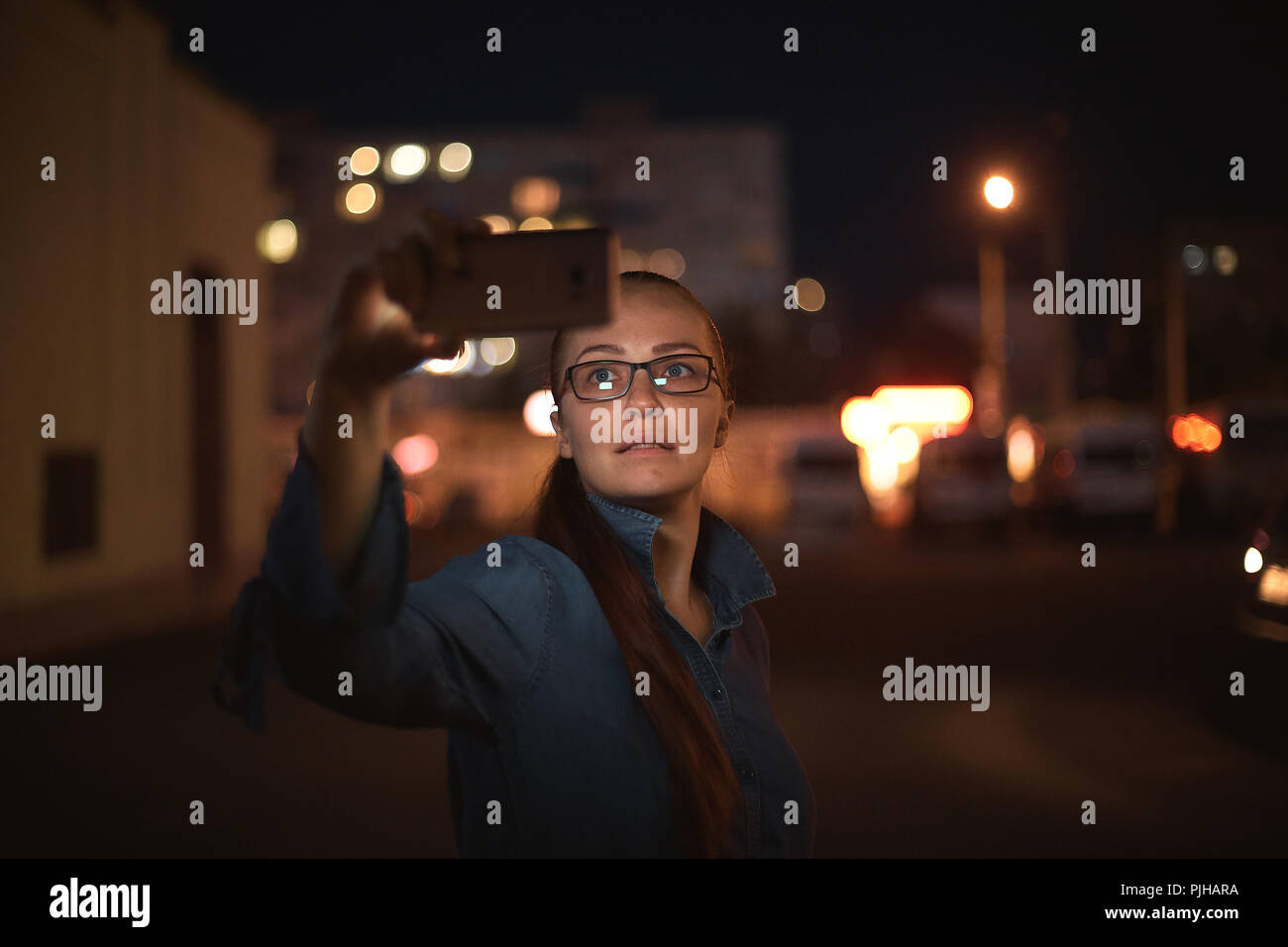Portrait of young beautiful caucasian woman using smart phone hand hold outdoor in the city night, smiling, face illuminated screenlight - social network, technology, comunication concept Stock Photo