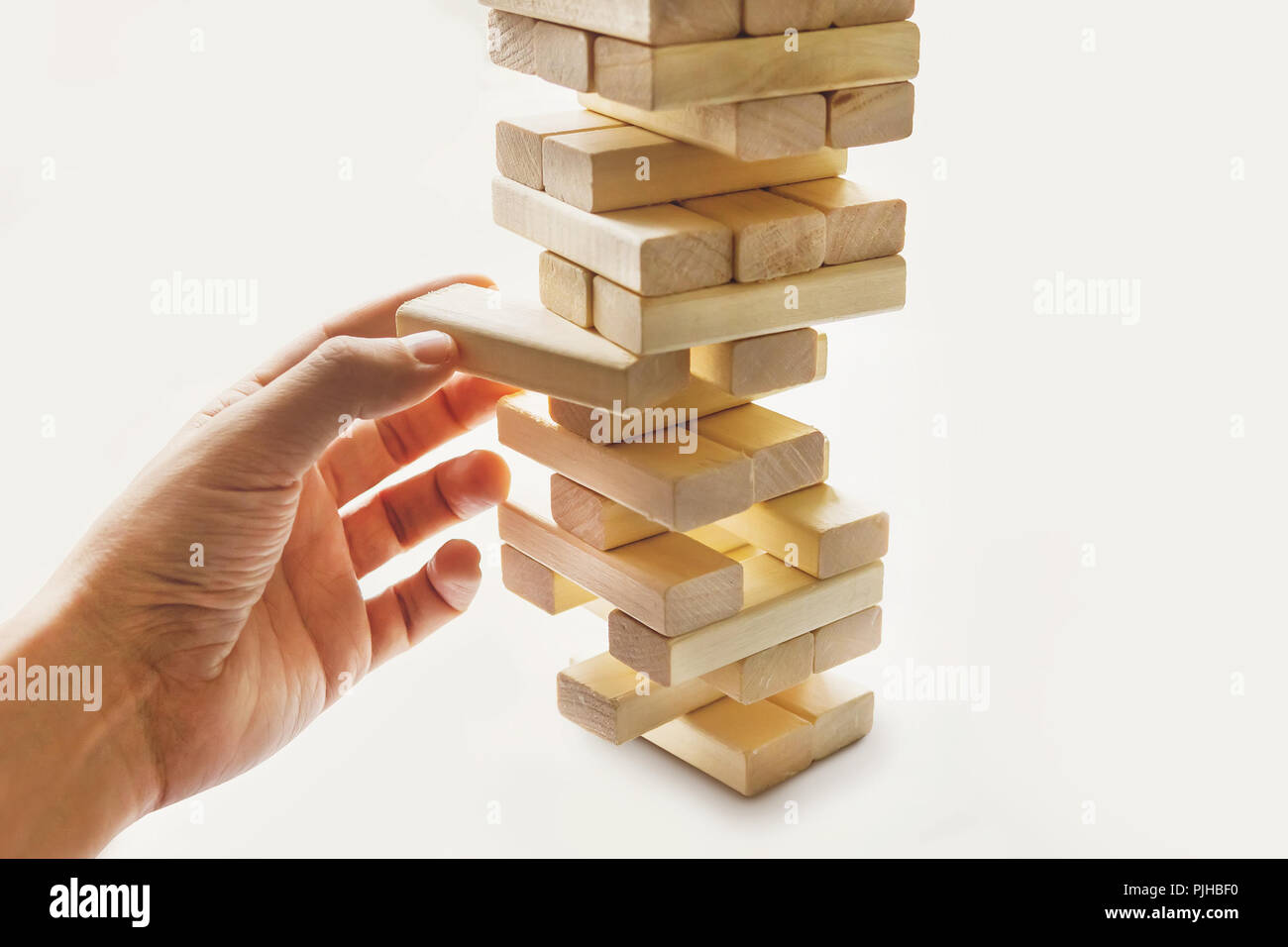 The tower from wooden blocks and man's hand take one block. The game of dice on white background.. Stock Photo