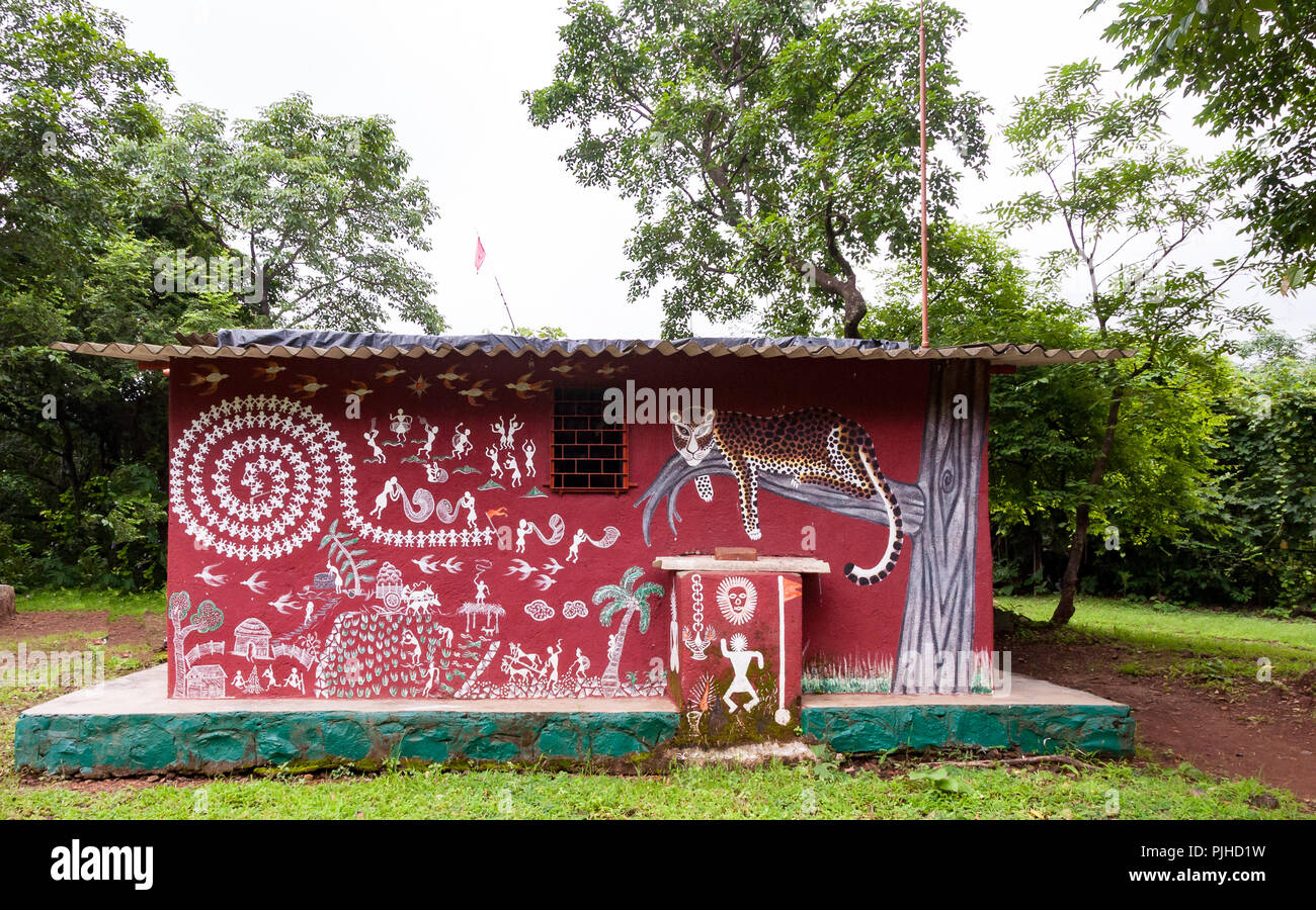 MUMBAI, INDIA – August 9 2018: Colourful mural on a Warli temple, surrounded by trees. Shows traditional scenes of farming, domestic animals, village  Stock Photo