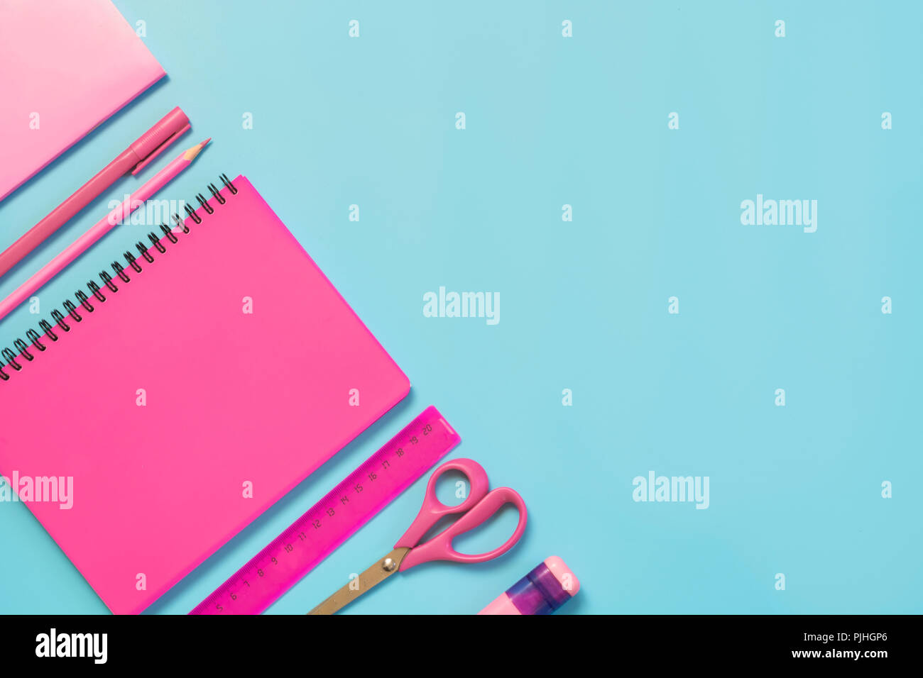 Pink girlish school supplies, notebooks and pens on punchy blue