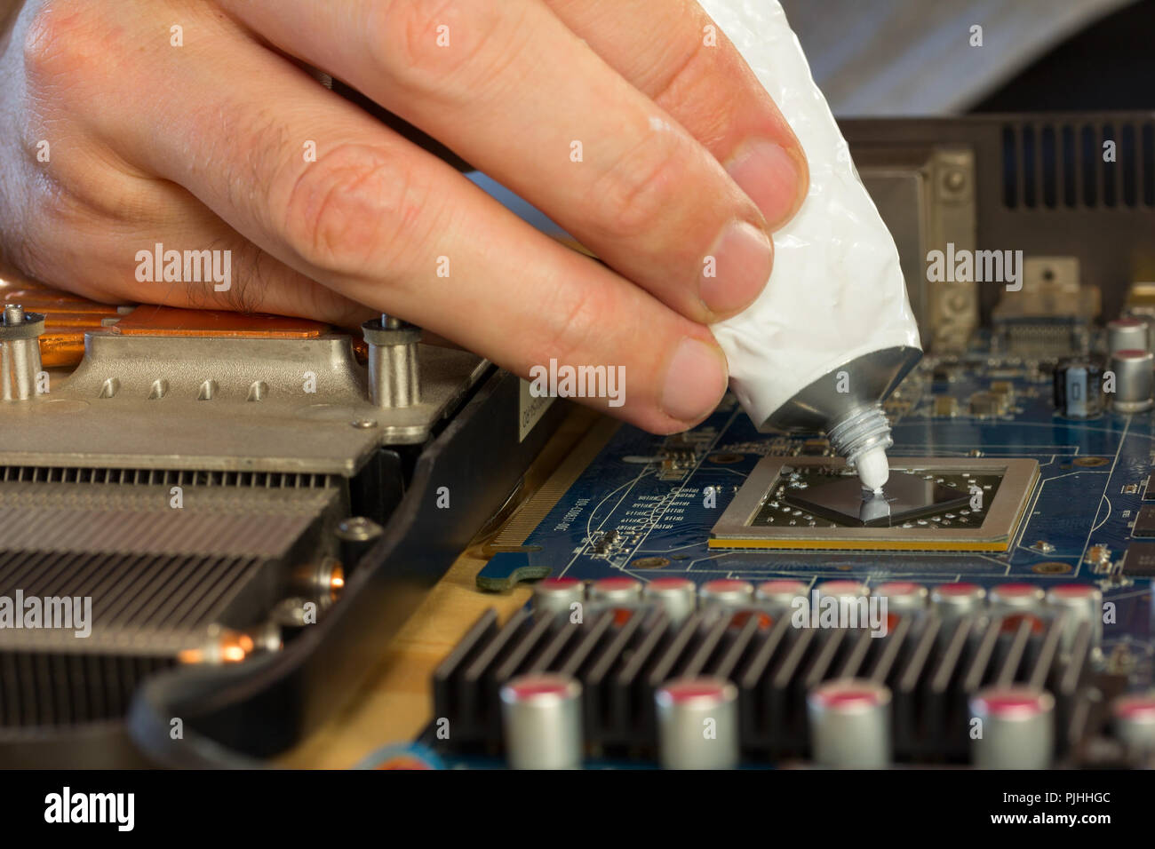 computer repair. men's fingers squeezed from a tube of thermal paste to the video processor