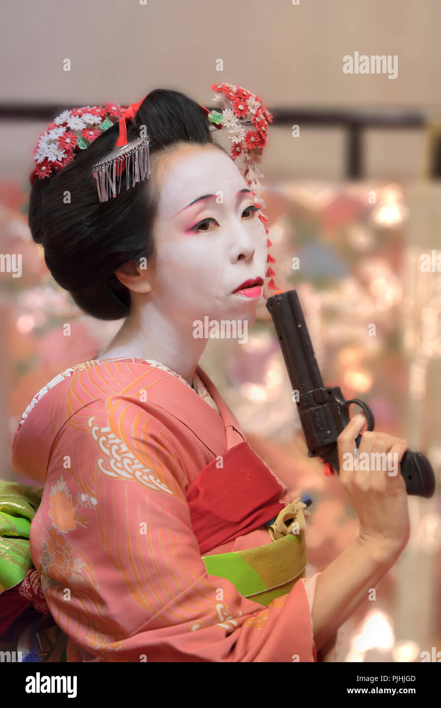 Pretty young Geisha maiko girl in kimono holding a plastic gun in her hand. Stock Photo