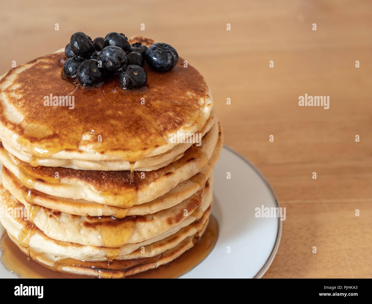 A large stack of pancakes covered with maple syrup and blue berries Stock Photo
