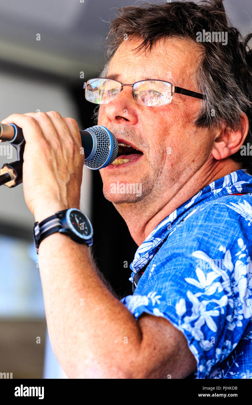 Close up of caucasian man, face, 40s, holding microphone on stand and singing or talking. Wears glasses and blue shirt. Stock Photo