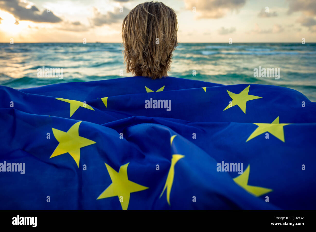 Man holding a fluttering iconic EU flag with circle of stars on beach at sunrise Stock Photo