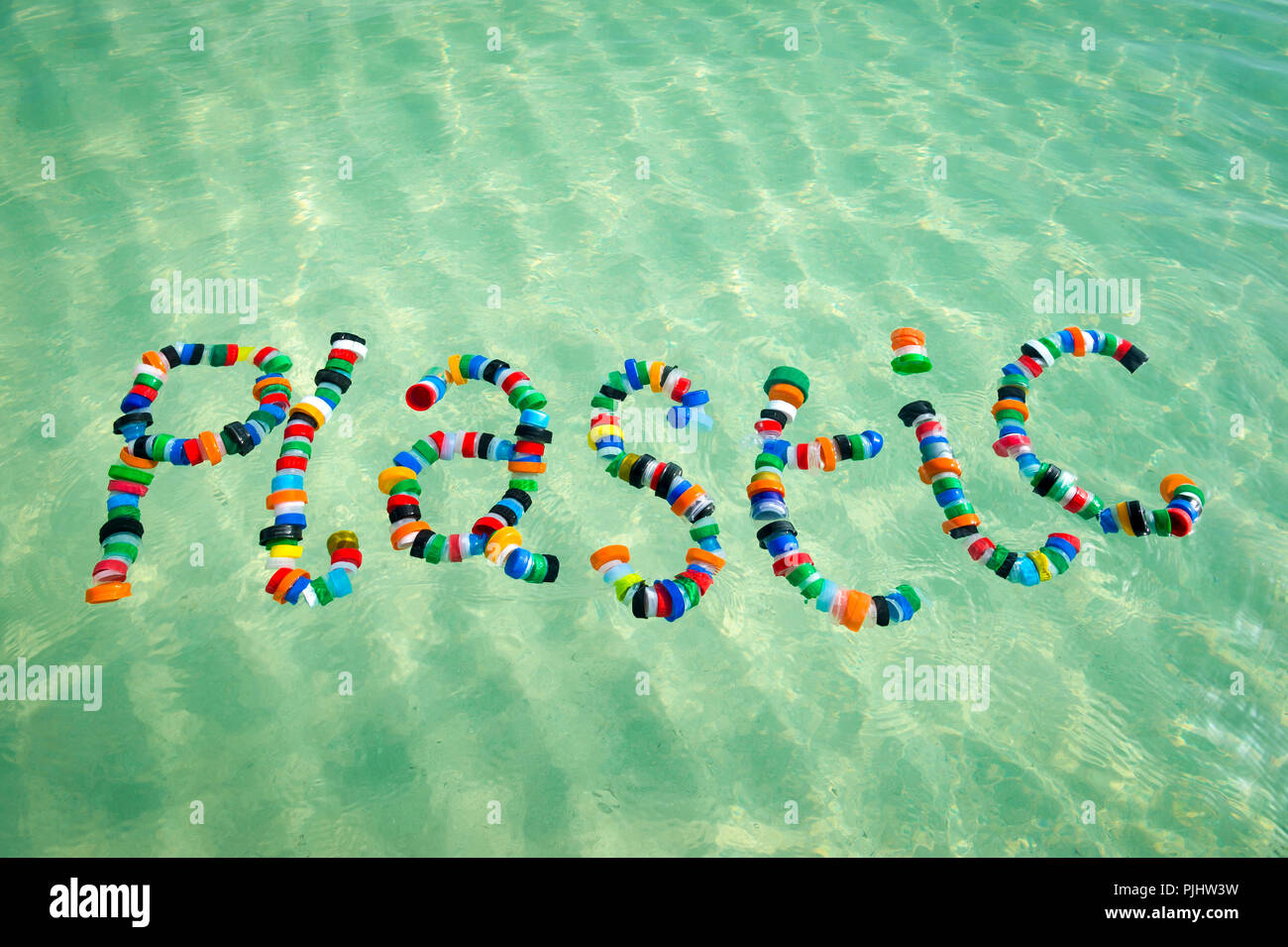Colorful bottle caps spell out the word 'plastic' floating on the sea. A reminder for people to reduce, reuse and recycle. Stock Photo