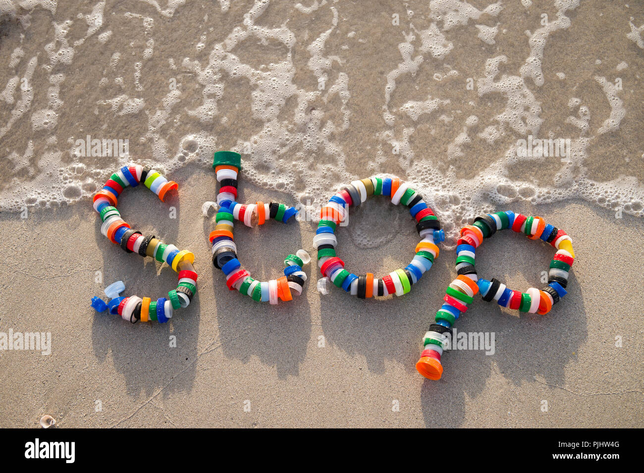 Colorful plastic bottle caps spell out the word 'stop' floating on a beach. A reminder for people to reduce, reuse and recycle. Stock Photo