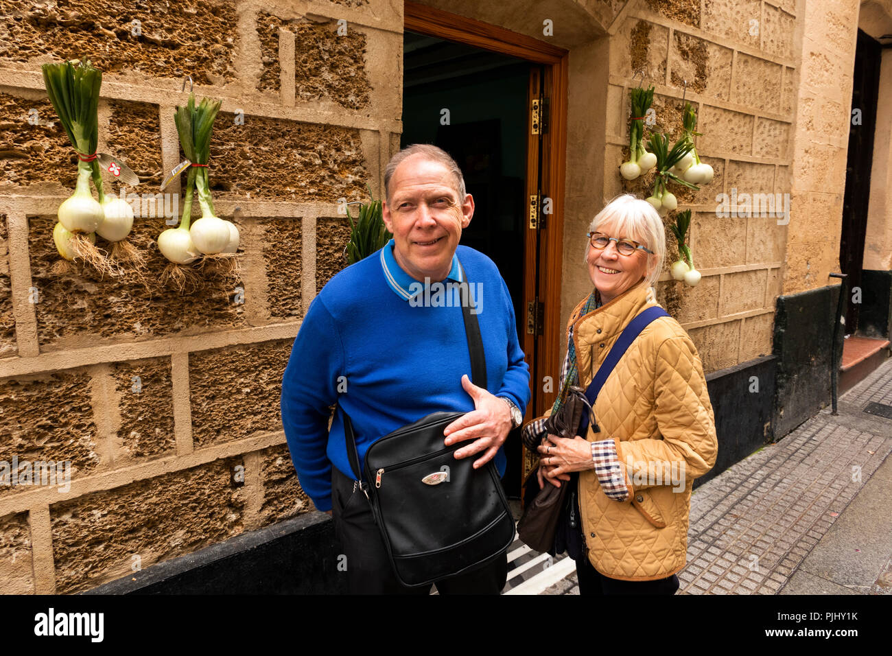 Spain, Cadiz, Calle Sopranis, happy tourists outside vegetable shop with onions outside Stock Photo