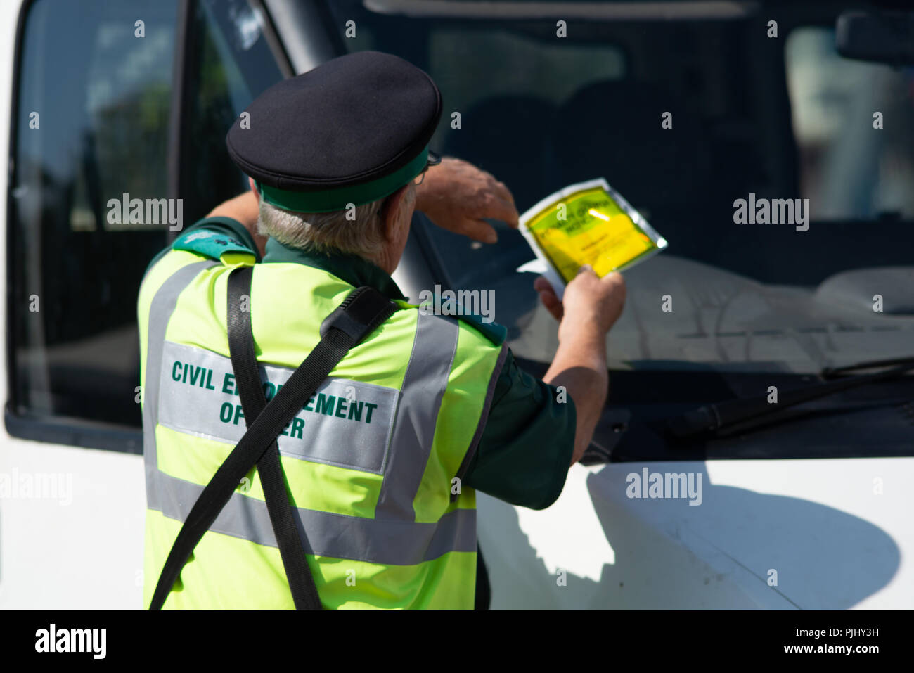 traffic warden civil enforcement officer wearing reflective yellow vest issuing fixed penalty parking ticket fine to white van Stock Photo