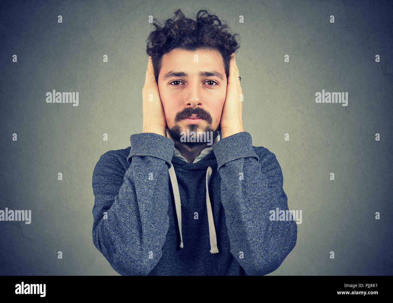 Young man covering ears avoiding noise on gray background Stock Photo