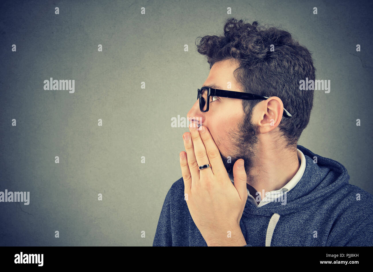 Young man covering mouth while gossiping and telling secrets in whisper. Stock Photo