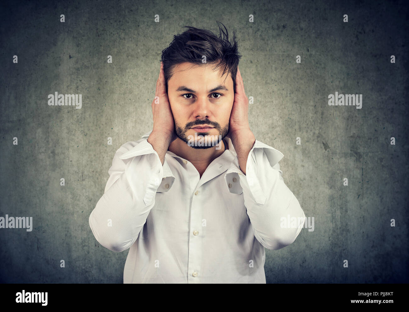 Young man covering ears avoiding noise on gray background Stock Photo