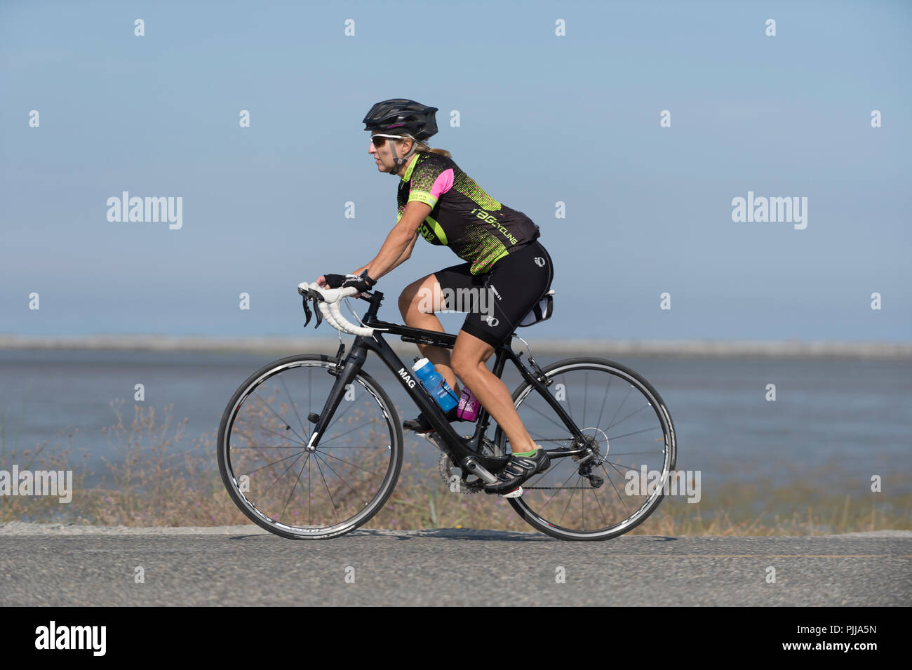 Female bicyclist wearing a helmet, cycling down a roadway. Stock Photo