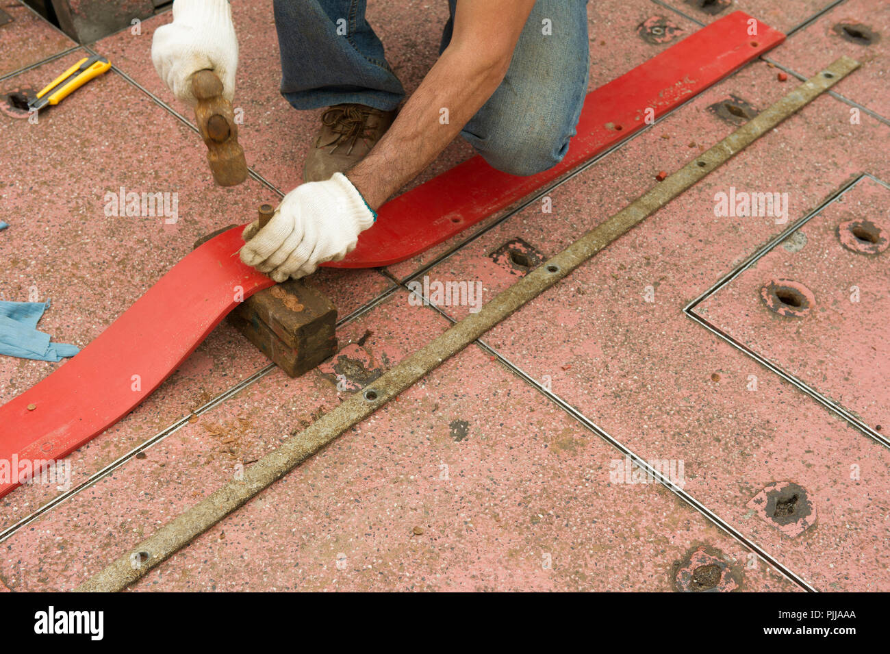 Worker wearing gloves, punching holes in leather strap, with hammer and