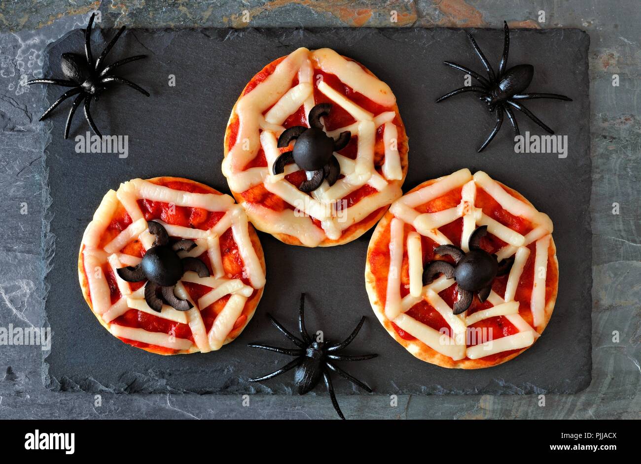 Halloween spider web mini pizzas, overhead view on a slate server with spiders Stock Photo