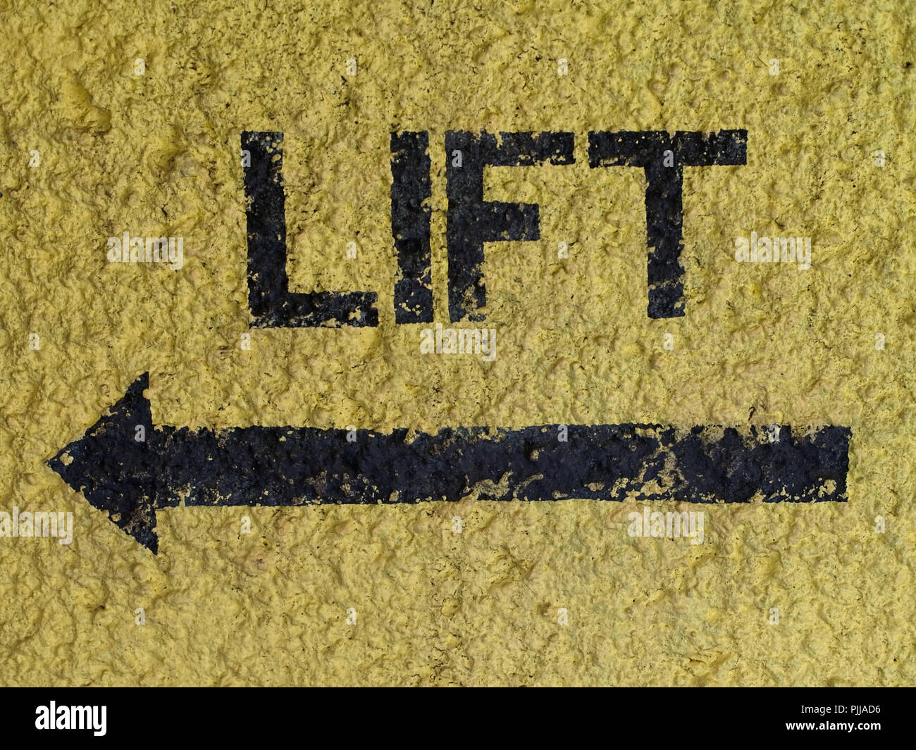Word "LIFT" and arrow painted in black on yellow wall pointing at the