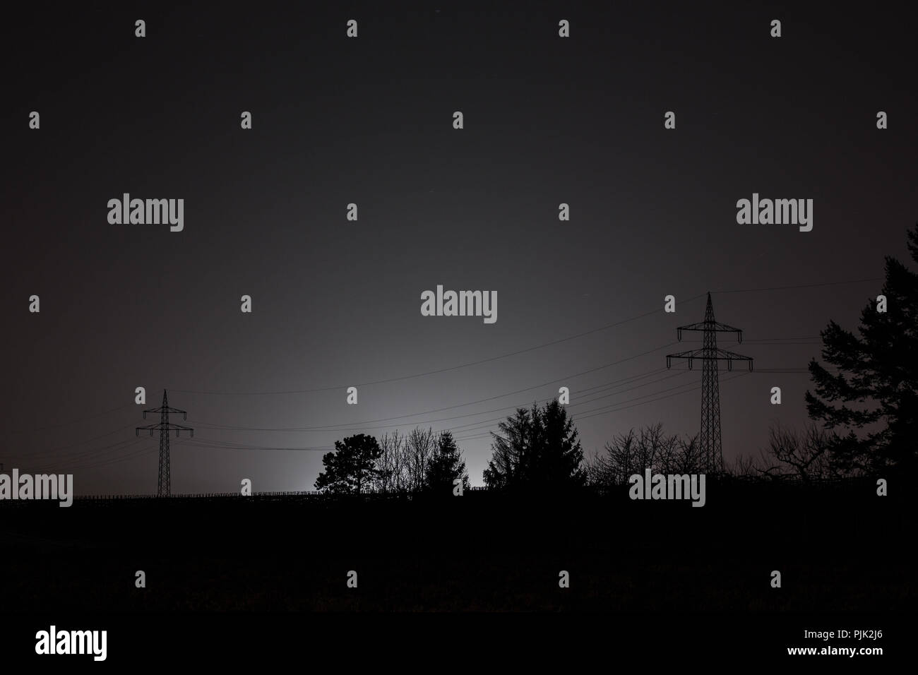 Silhouettes of trees and electricity pylons in a bright glow, contours, dark, black and white Stock Photo