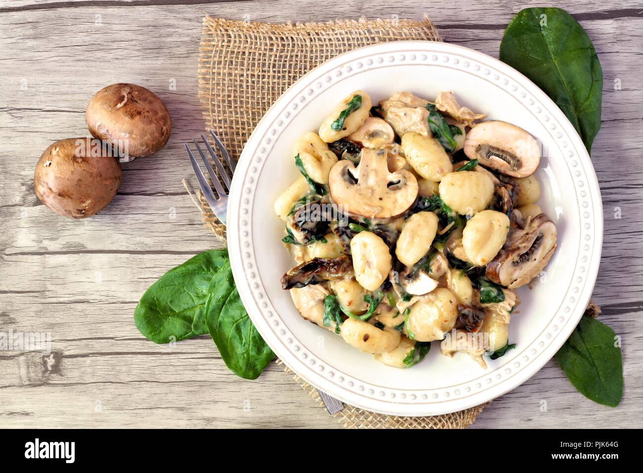 Gnocchi with a mushroom cream sauce, spinach, chicken and sun dried tomatoes, above scene on a wood background Stock Photo