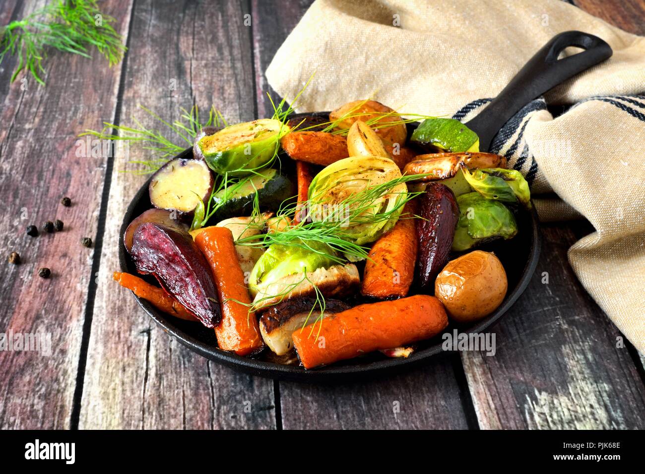 Cast iron skillet of roasted autumn vegetables, against a rustic wood