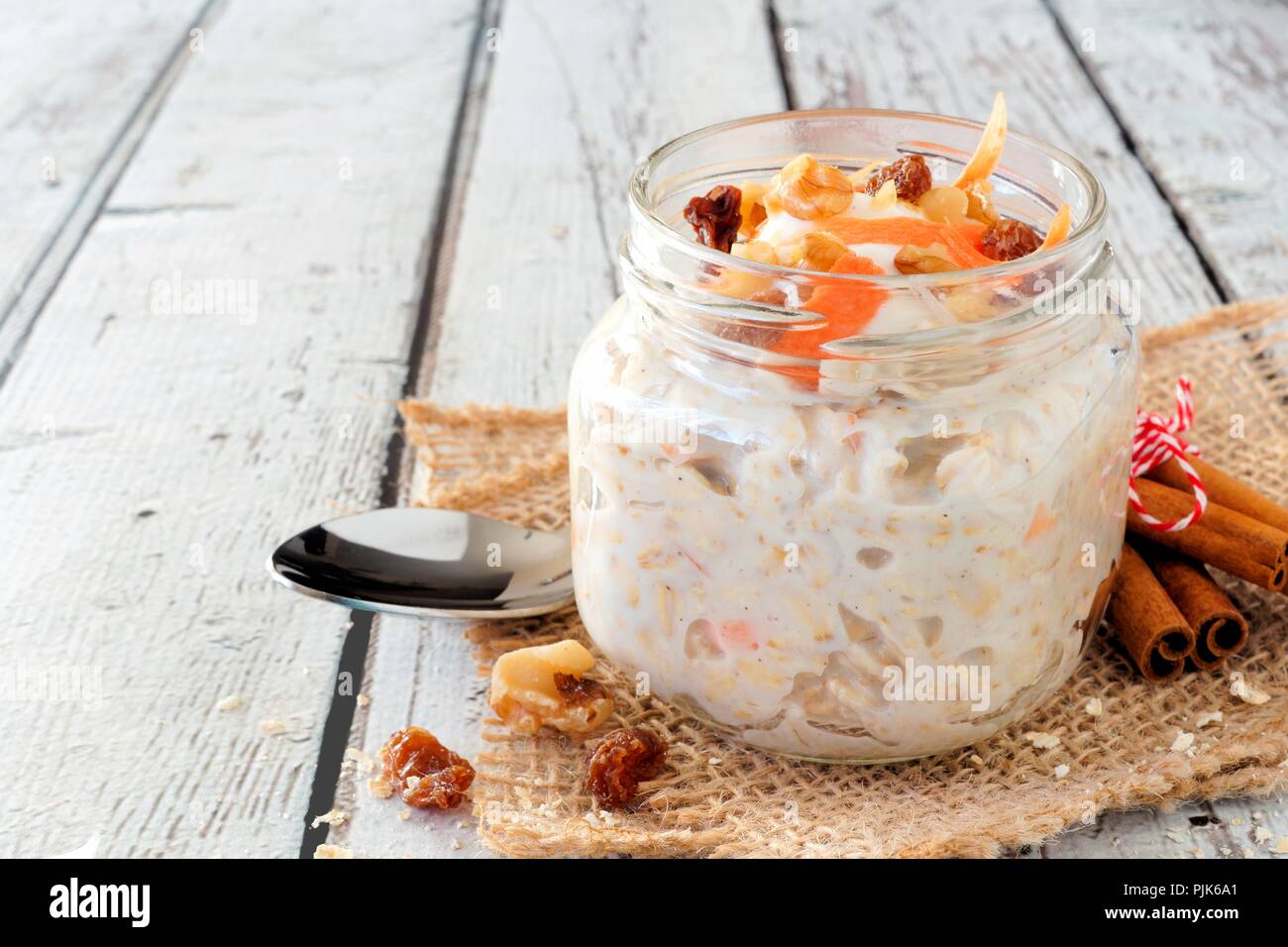 Carrot cake overnight oats with nuts and raisins in a mason jar on a rustic white wood background Stock Photo