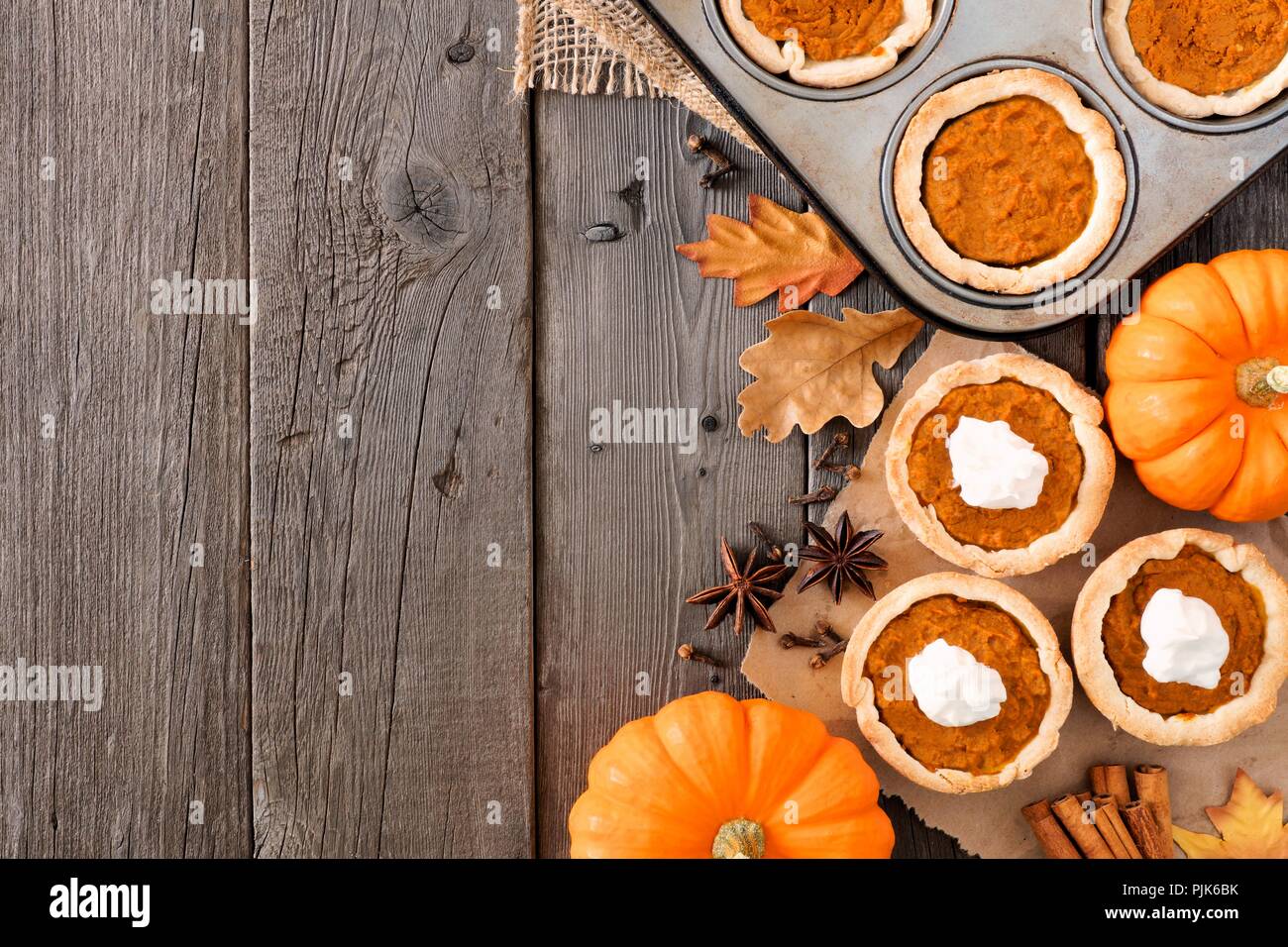 Autumn baking scene side border with pumpkin tarts over a wood background Stock Photo