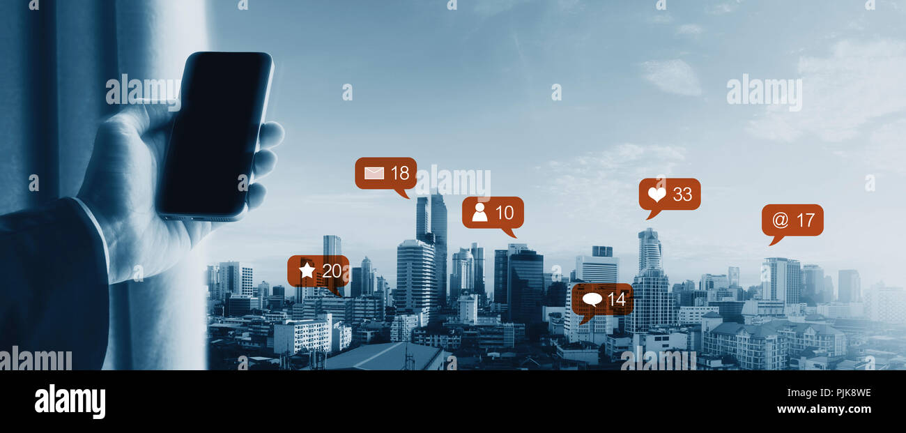 Hand using mobile smart phone, with notification icons and city skyline view. Social network, connection and e-commerce business Stock Photo