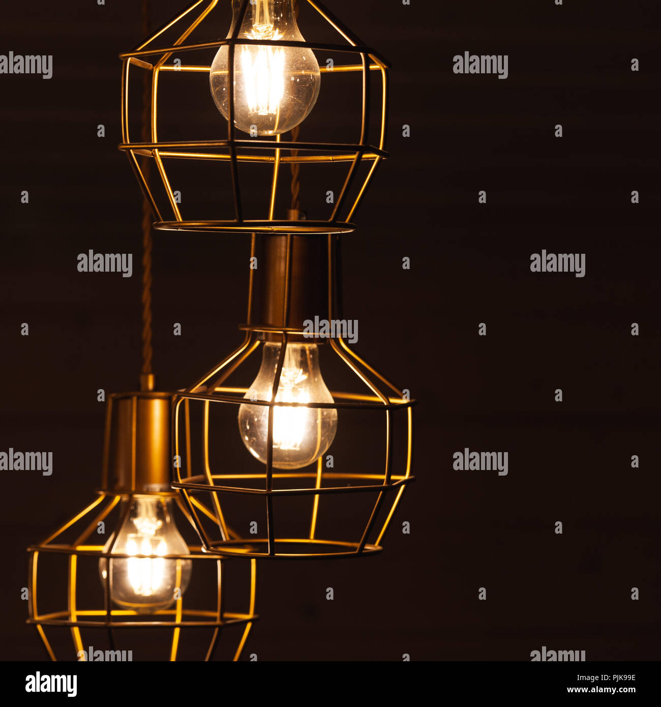 Ceiling chandelier with hanging three bulb lamps, yellow LED lighting elements covered with metal wire frame lampshades, square framed photo with sele Stock Photo