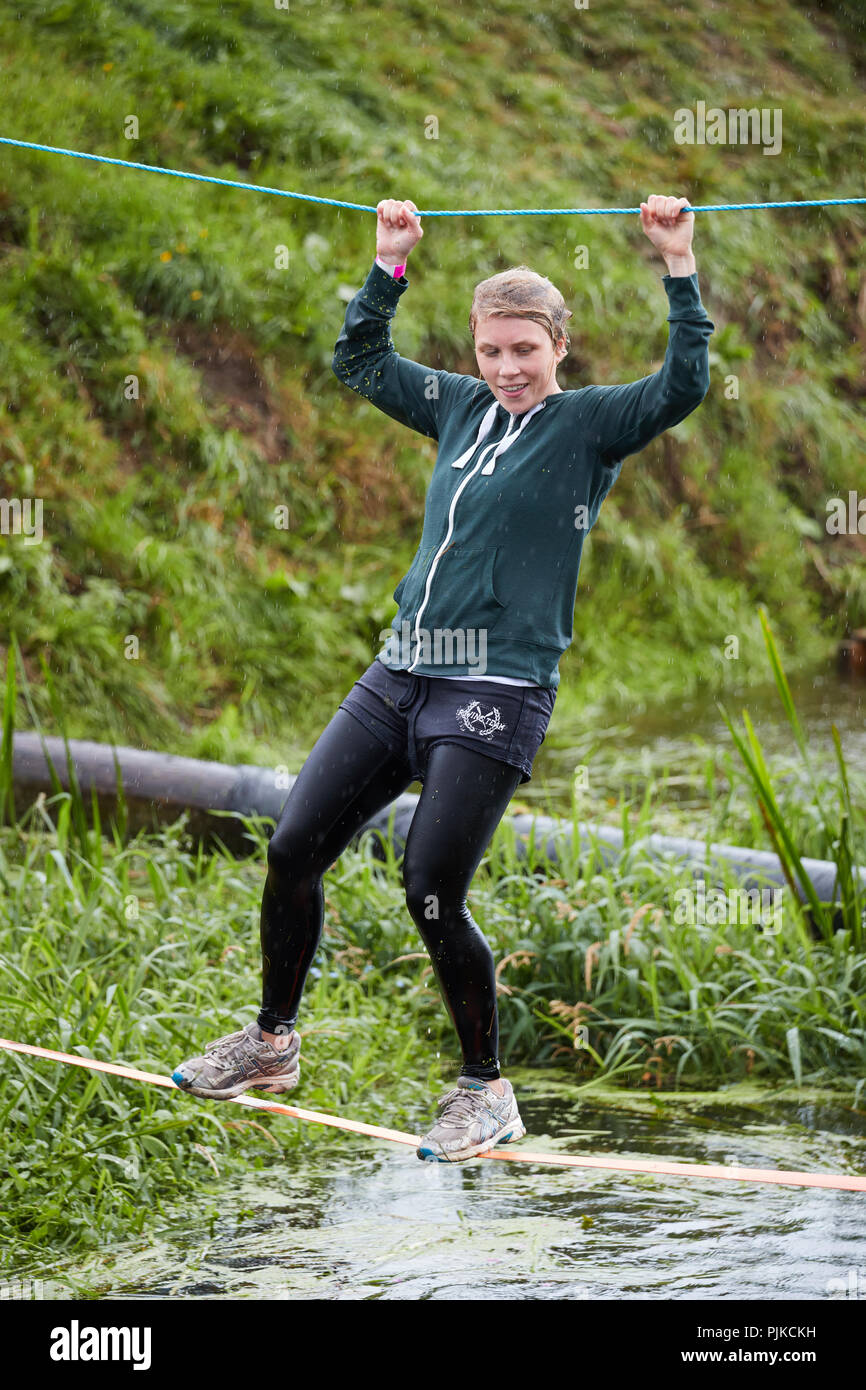 A wet young girl walking along a slack line over a water obstacle course at The Lowland Games, Thorney, Somerset, England Stock Photo