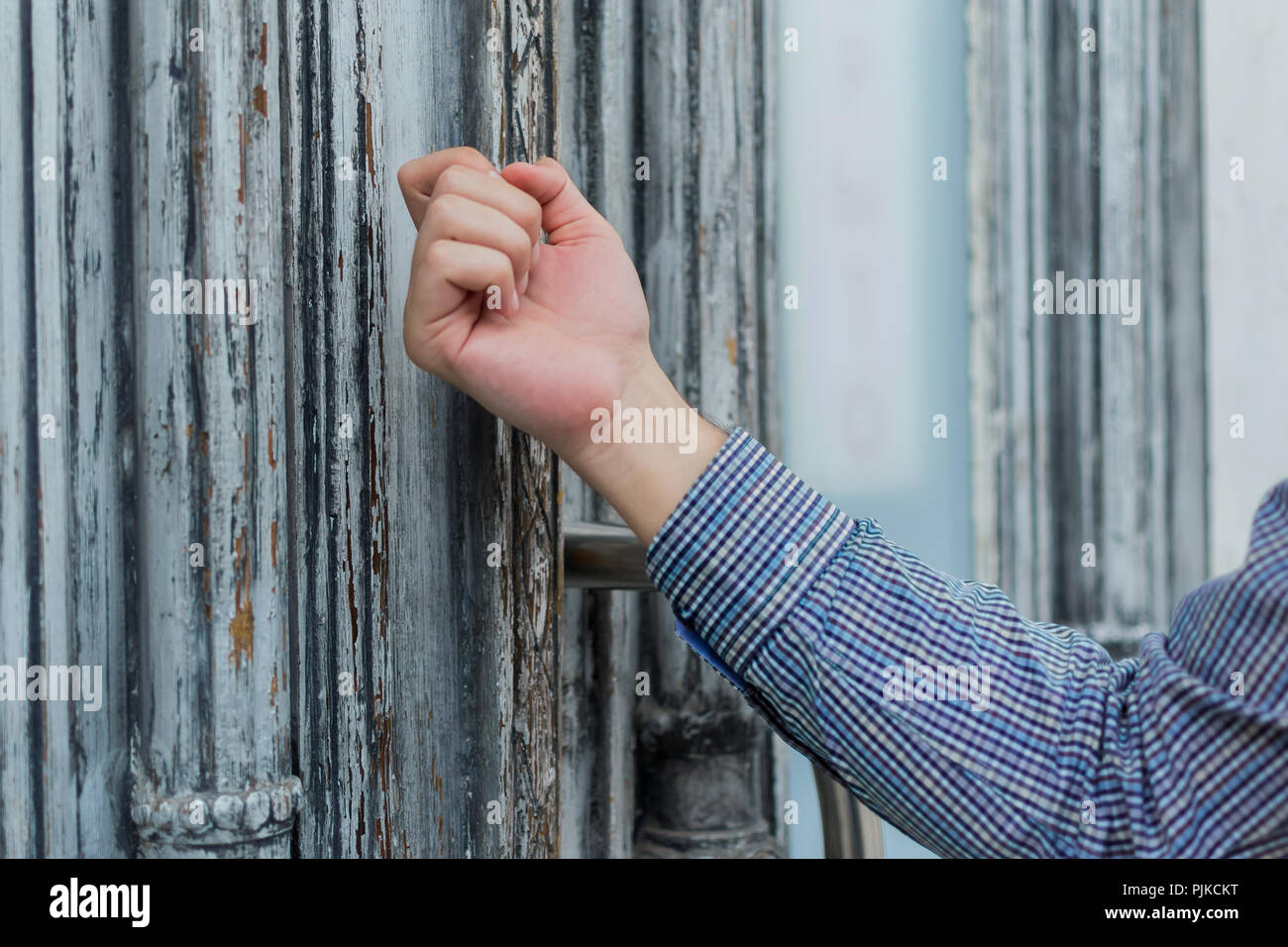 hand realtor in a plaid shirt knocking his fist at the old and shabby front door. Anybody home. Stock Photo