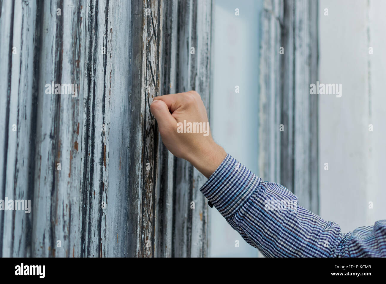 hand postman in a plaid shirt knocking his fist at the old and shabby front door. Anybody home. Stock Photo