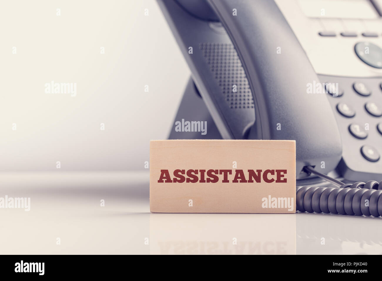 Retro image of support concept with a small wooden sign saying - Assistance - standing alongside a telephone instrument with copyspace. Stock Photo