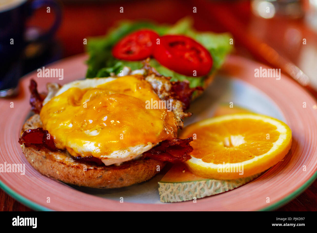 Breakfast toasted bagel bun served with bacon, sausage and egg sandwich with fruits. Stock Photo