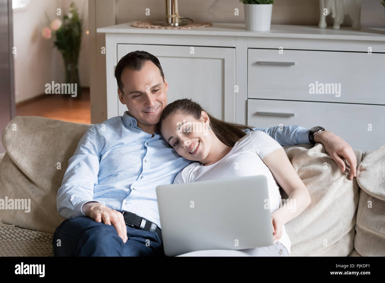 Loving couple cuddle on couch watching video on laptop Stock Photo