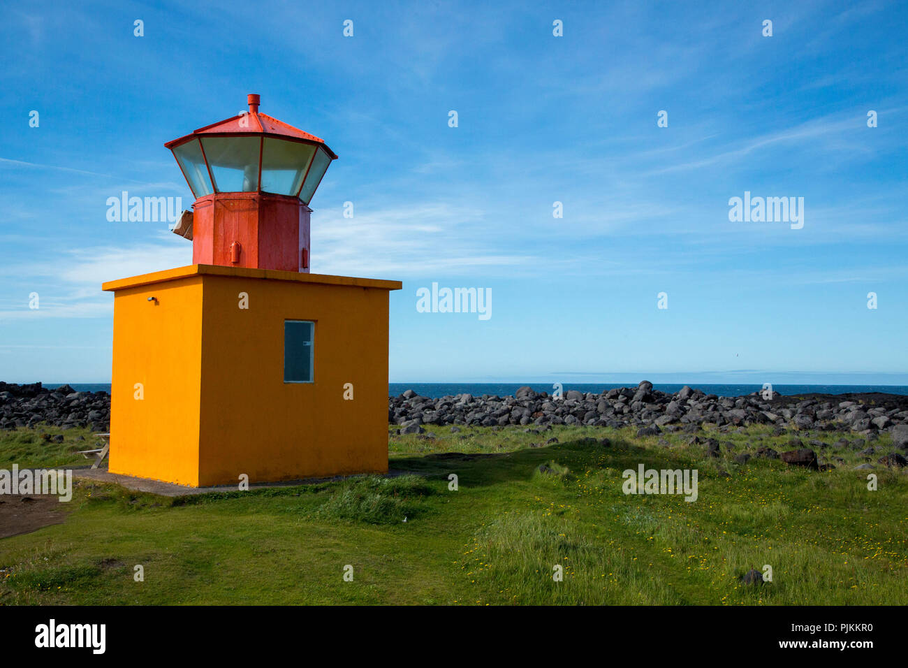 Iceland, small yellow lighthouse at Hellissandur, red roof, Snaefellsness peninsula, stone wall, sea in the background Stock Photo