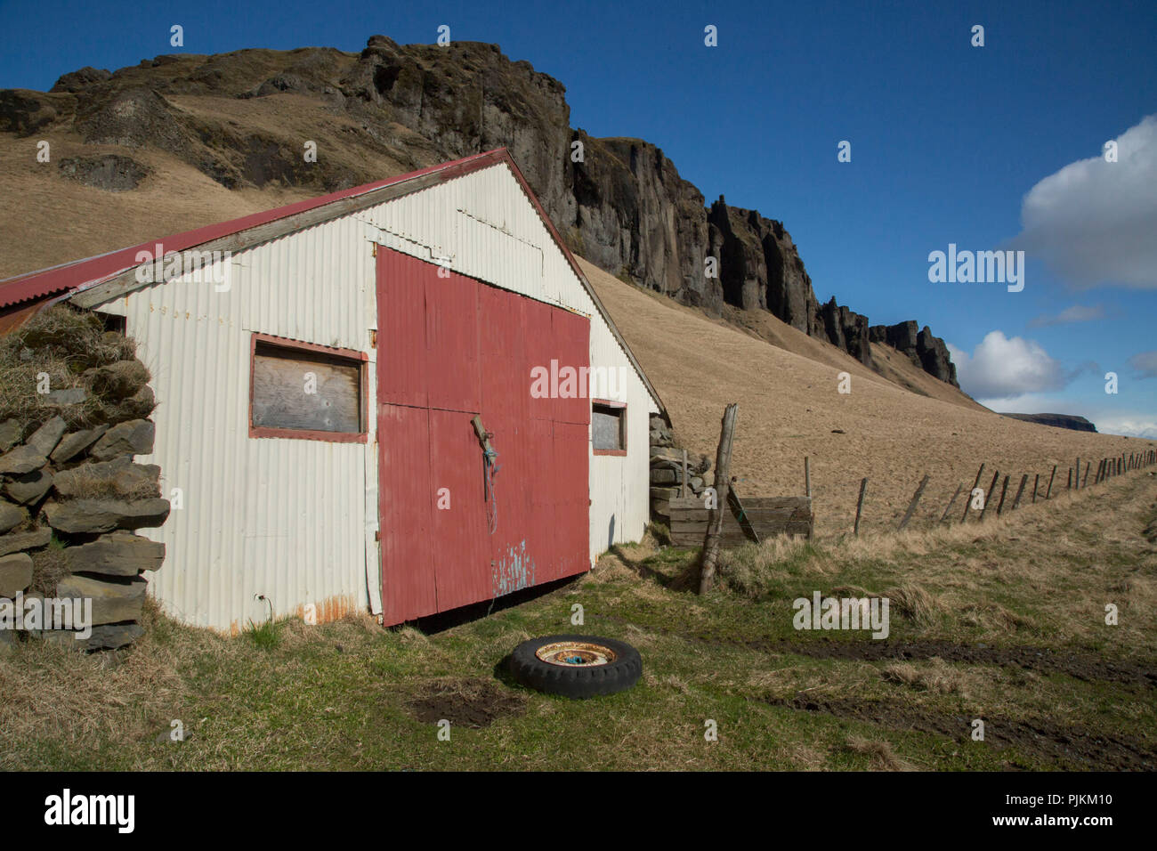 Iceland, south Iceland, old barn with car tire, fence, mountains, blue sky Stock Photo
