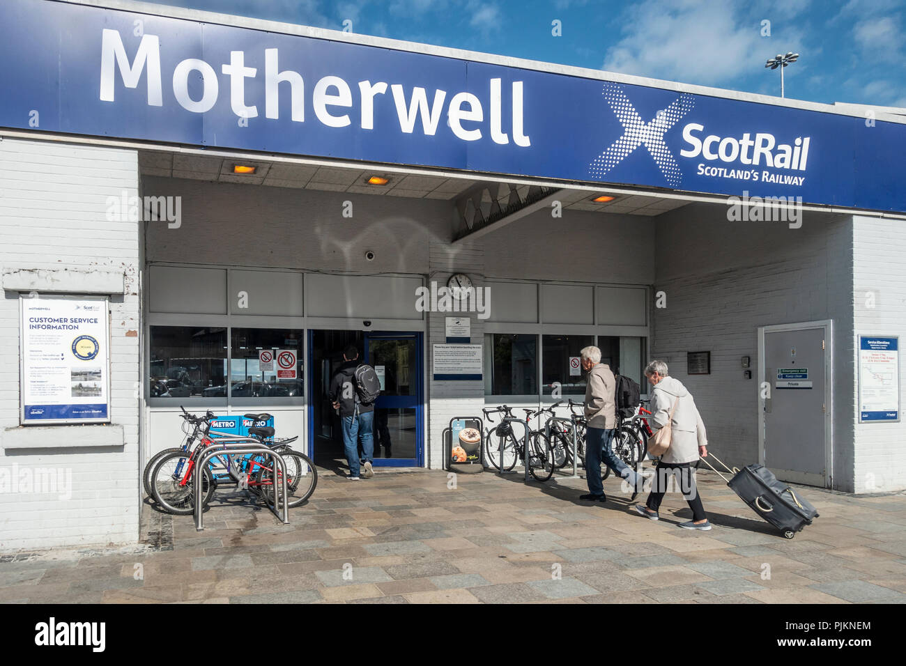 Passengers entering Motherwell ScotRail railway station. Two men with rucksacks, one woman pulling a suitcase on wheels. Bicycle racks. North Lanarksh Stock Photo