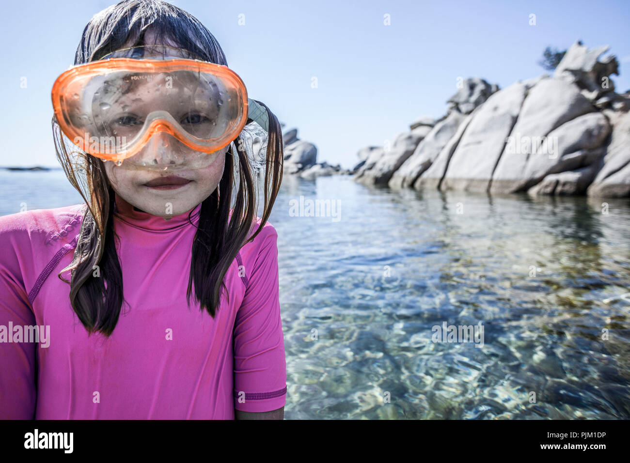 Girl with scuba mask in lonely rocky bay in front of crystal clear water. Stock Photo