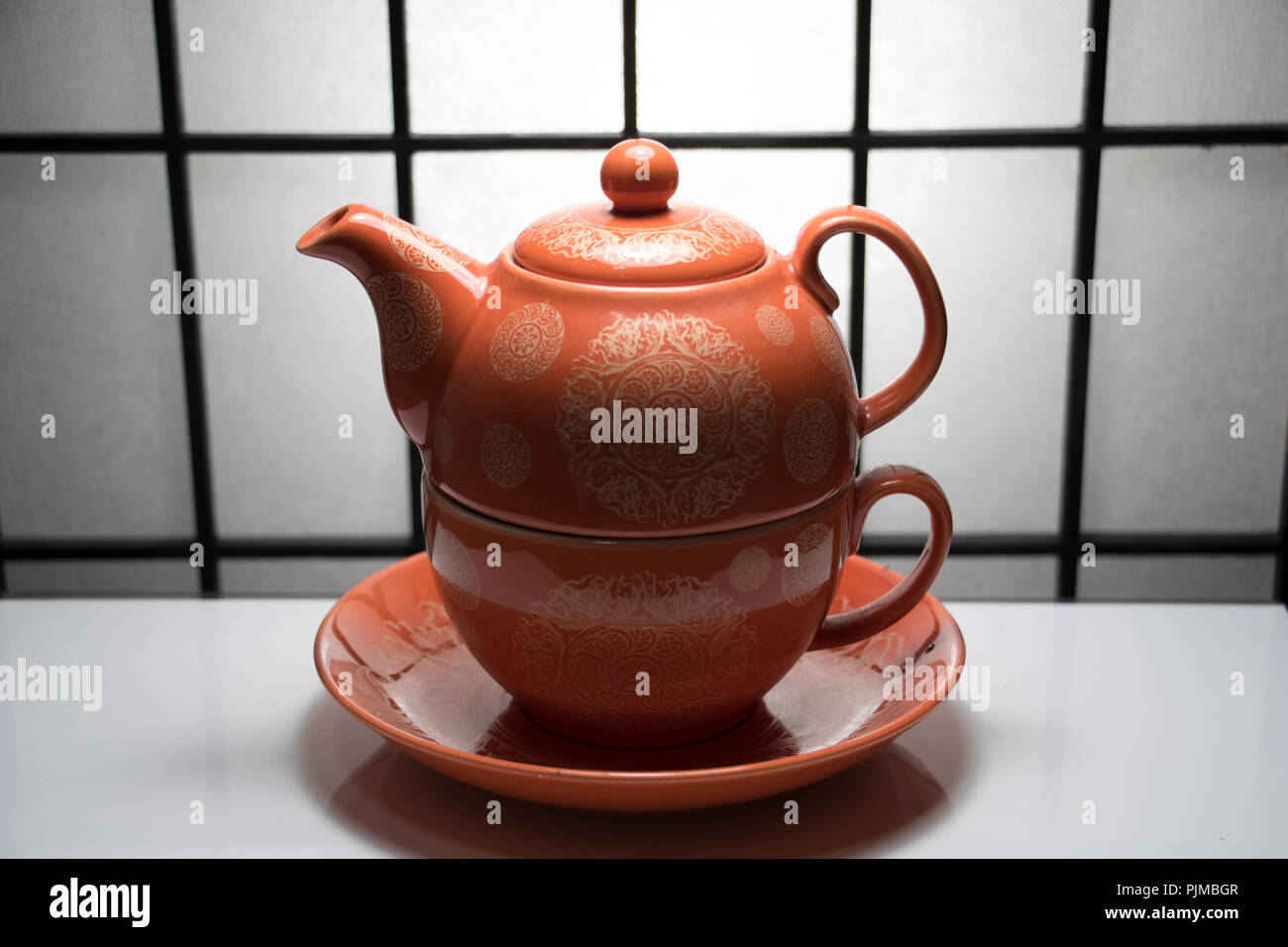 Japanese tea cup and kettle on a white shiny table with Asian paper dividing wall in the background. Stock Photo
