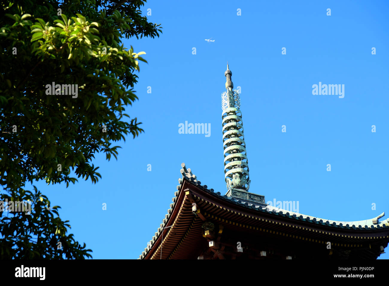 Jet soars above the decorated tip of the historical Kanei-ji Temple pagoda Stock Photo