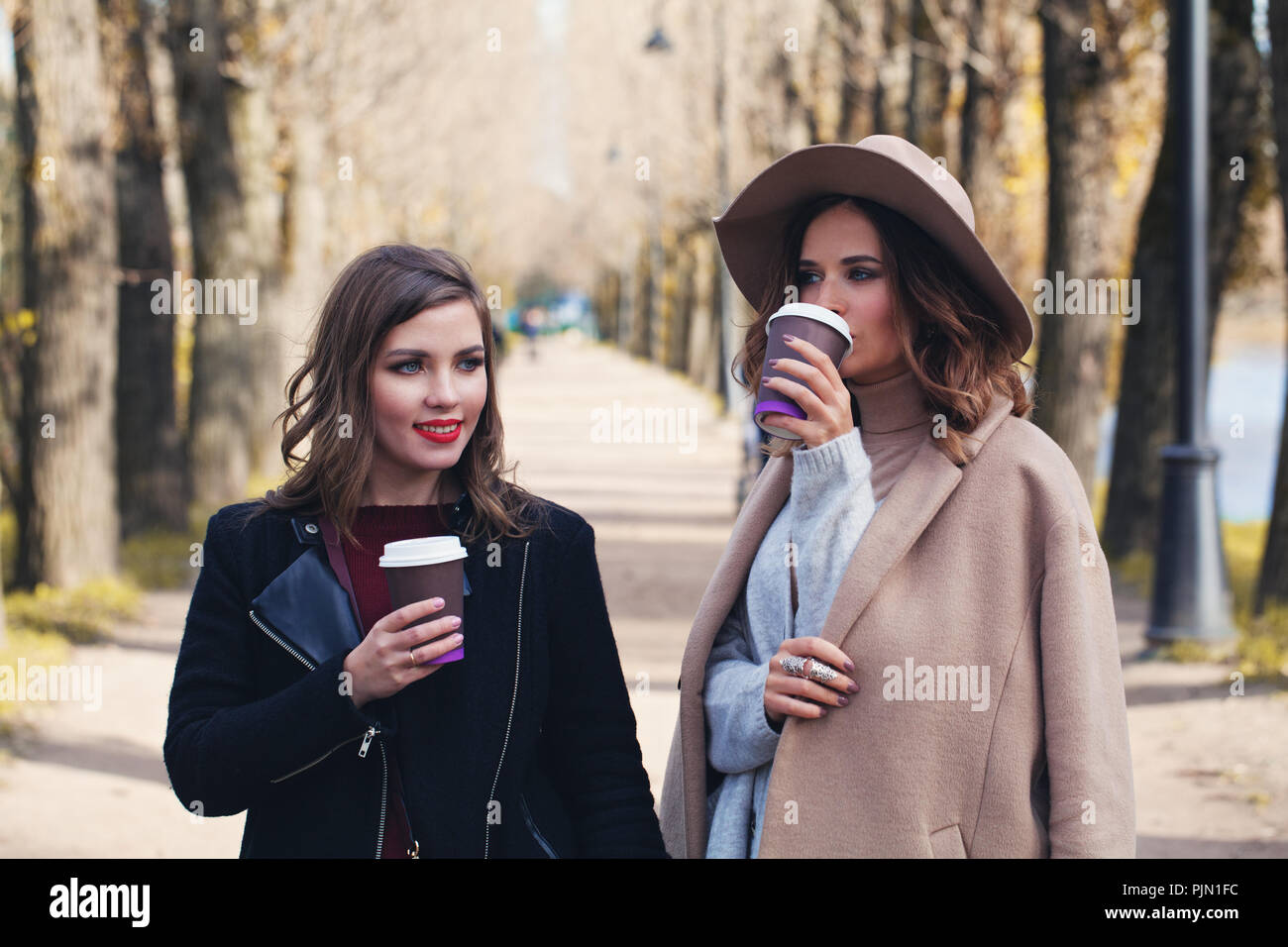 Happy women drinking cofee to go outdoors in autumn park Stock Photo