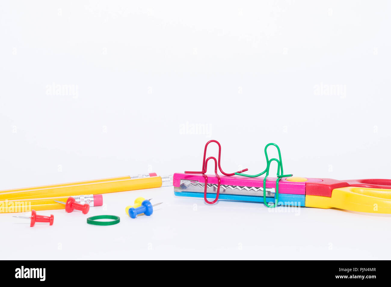 Two paper clips talking, sitting on a zigzag scissors with pencils in the background. Miniature school life and back to school concept with copy space Stock Photo