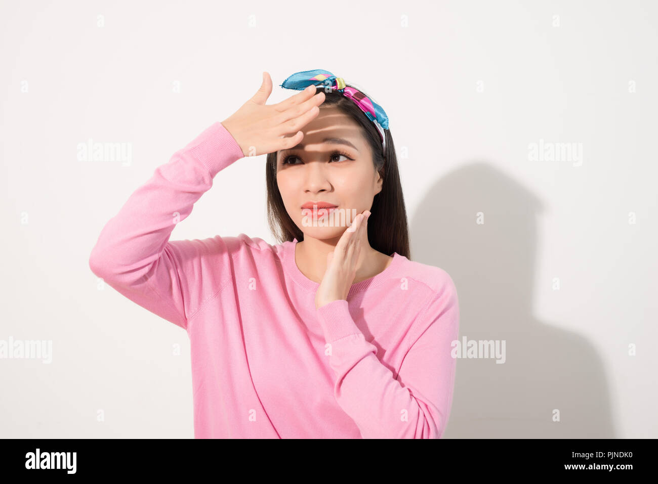 Portrait of a beautiful Asian girl  covering face by hand of bright sun light. Woman in a pink dress protecting her face from solar light. Skin care o Stock Photo