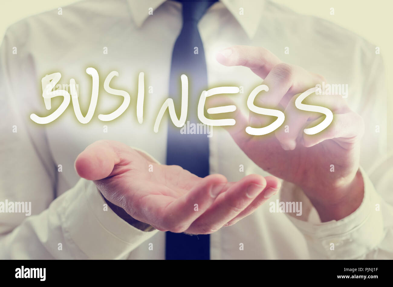 Business startup concept with the hands of a businessman reaching out to protect and activate the glowing word Business on a virtual screen or interfa Stock Photo