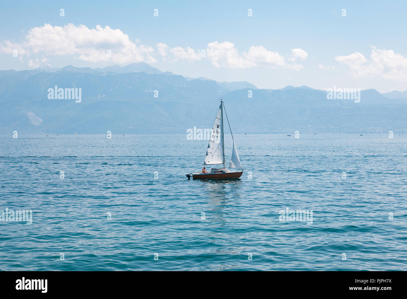 Small sail boat on Lake Leman (Geneva Lake) on beautiful sunny summer day with mountains and white clouds on the background Stock Photo