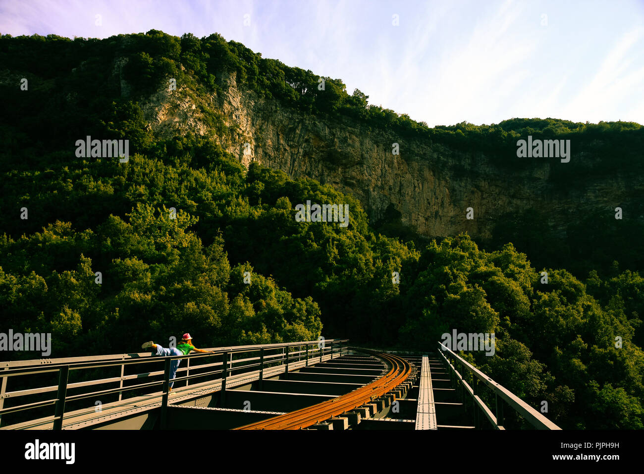 A woman wearing hat is doing yoga exercises on a steel railway bridge Stock Photo