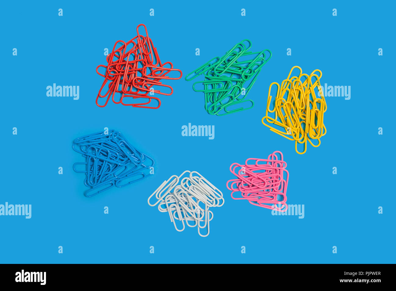 six heaps of different in colours paper clips lying on a blue background. free space for advertising text. top view. concept of office chancery Stock Photo