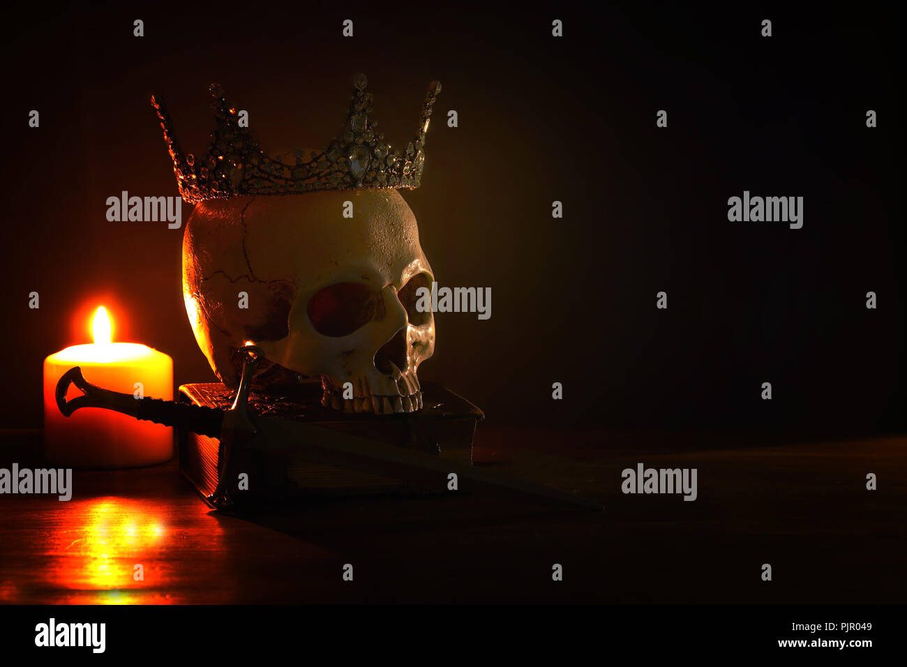 Human skull, old book, sword, crown and burning candle over old wooden table and dark background Stock Photo
