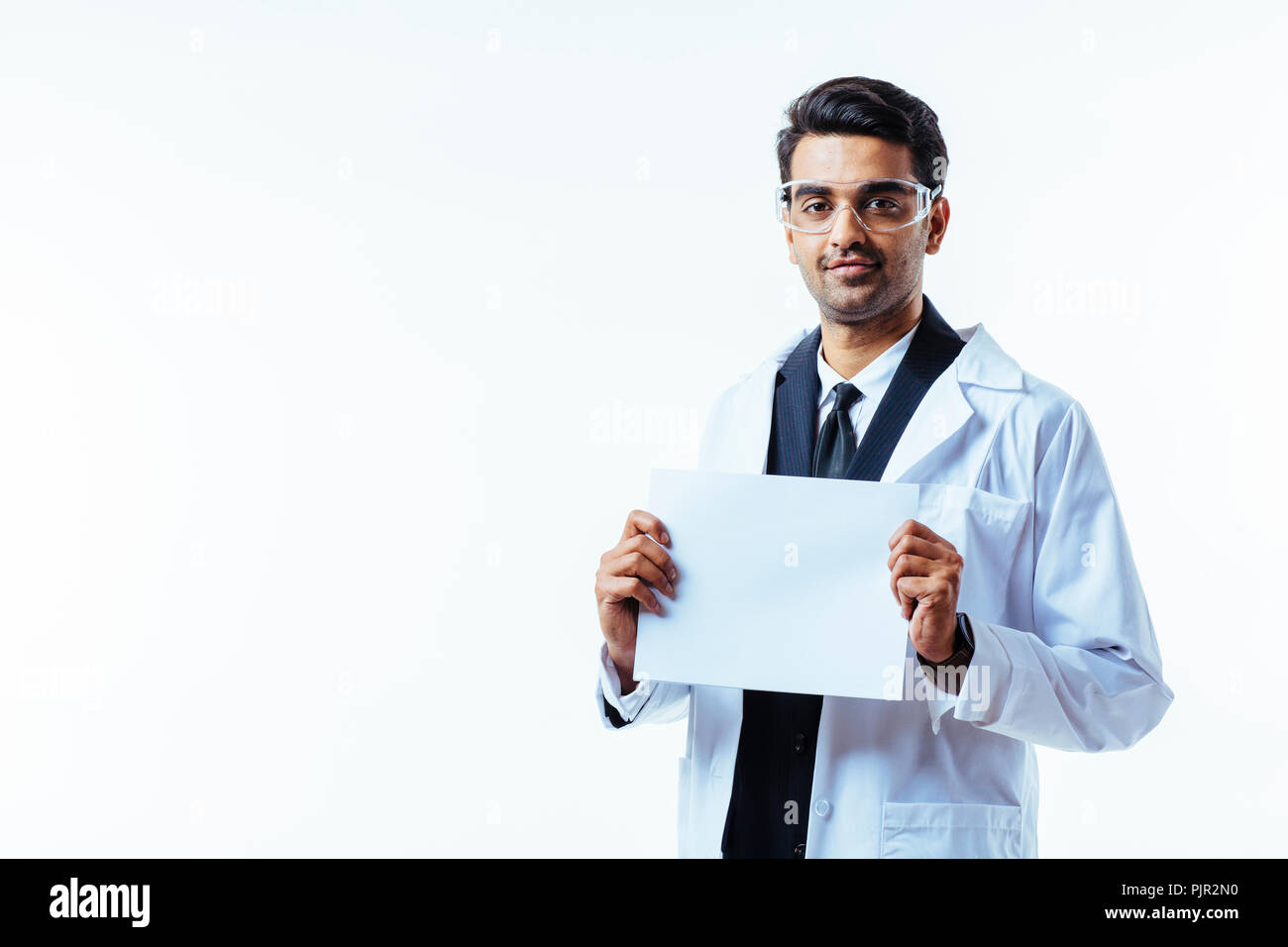 Portrait of a man in business suit, lab coat and protective glasses, looking at camera, holding a white cardboard, isolated on white studio background Stock Photo