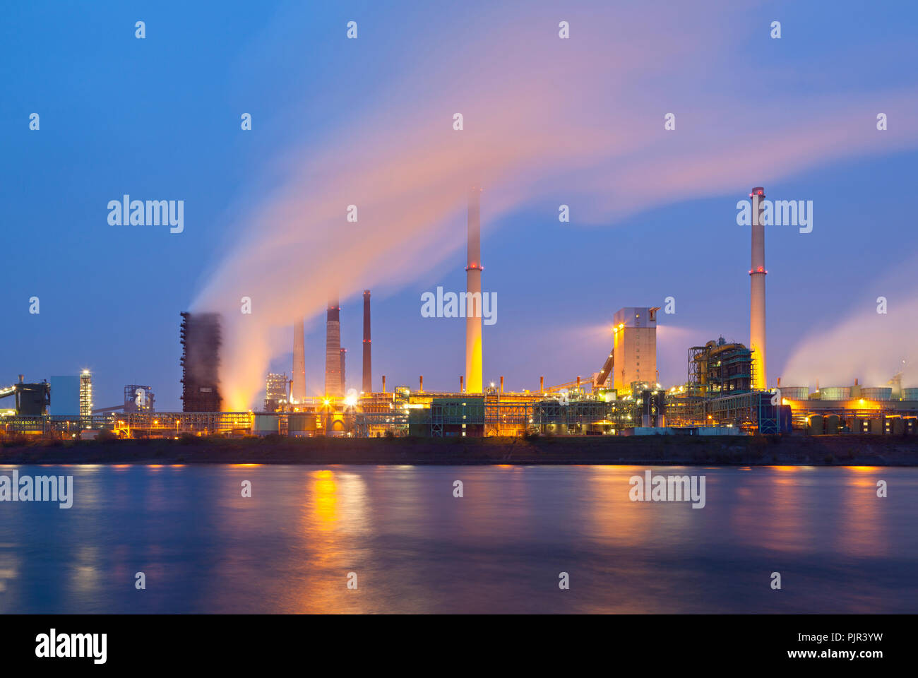 A coking plant seen over a river with a lot of steam and night blue sky. Stock Photo